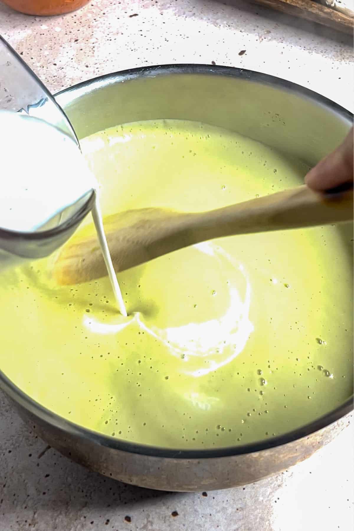 Adding cream to blended onion soup in a pot