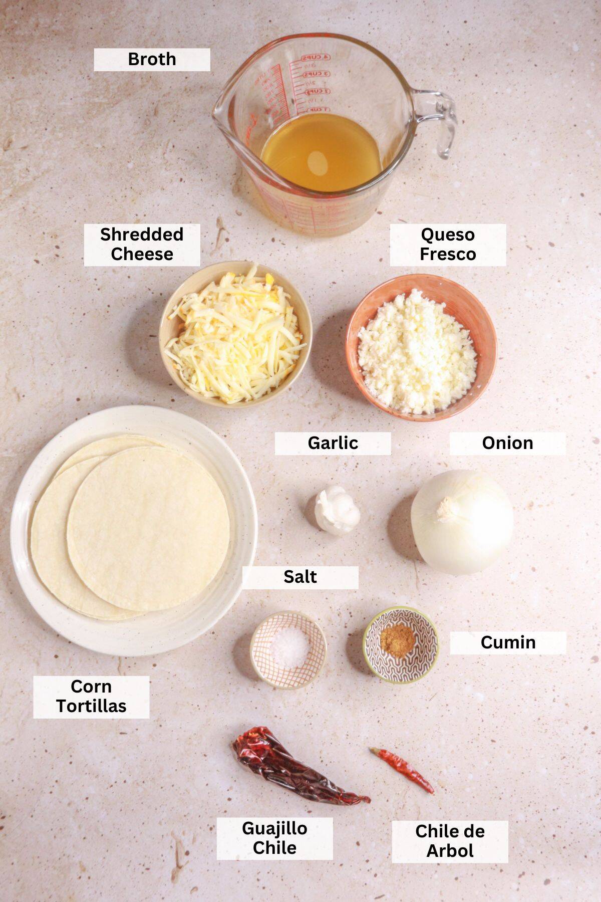 Ingredients for stacked enchiladas: broth, shredded cheese, peso fresco, corn tortillas, onion, garlic, salt, cumin, guajillo chile, chile de arbol