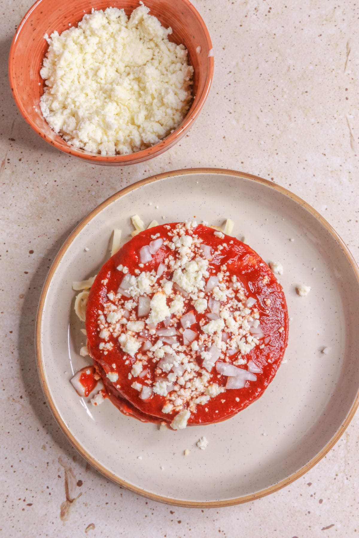 Last layer of stacked enchiladas topped with queso fresco and diced onion