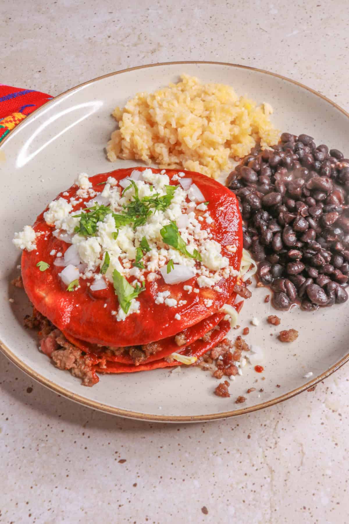 Variation of staked enchiladas with ground beef between layers and served with Mexican red rice and black beans