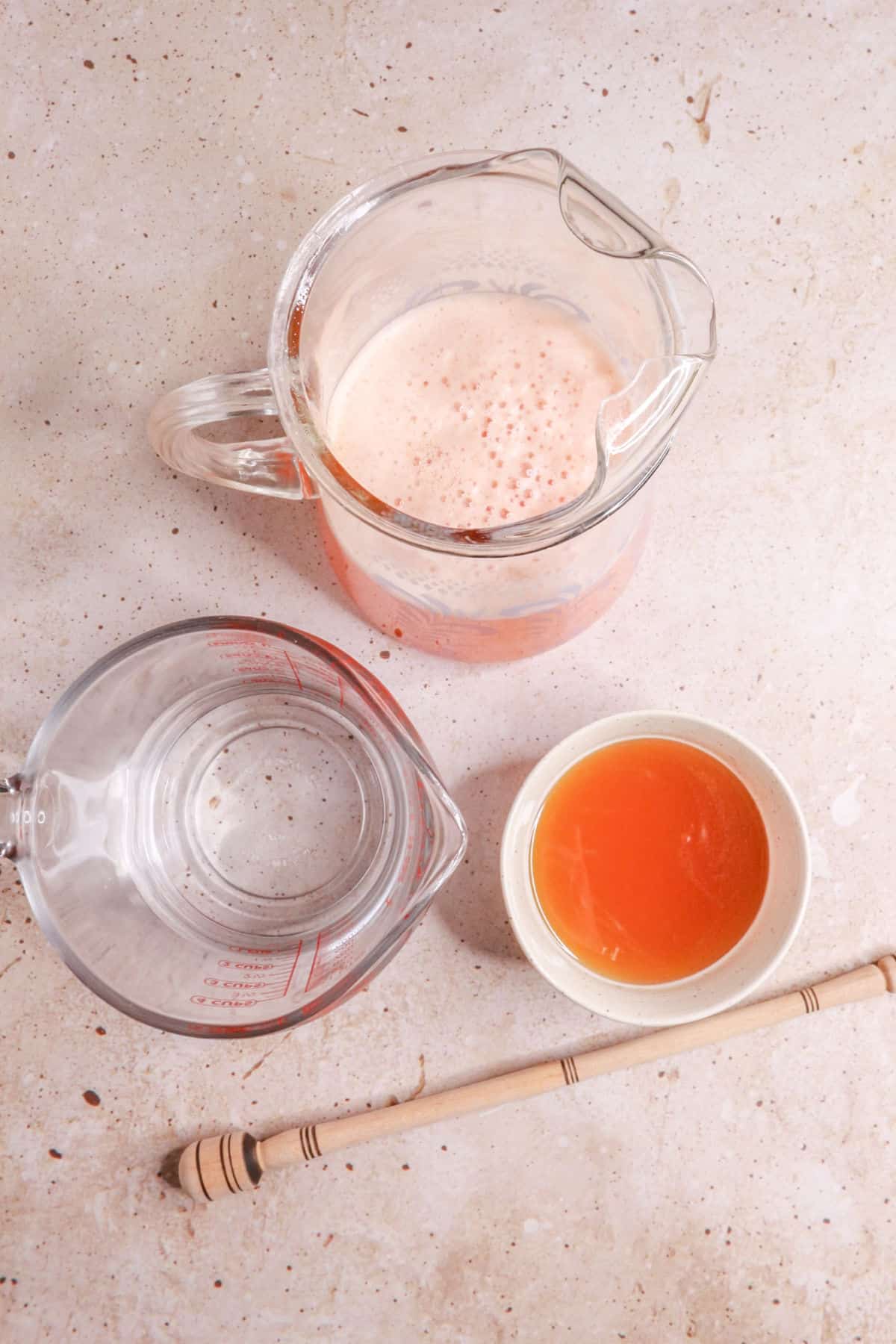Pitcher of agua de melon, a measuring cup with water, and a bowl with honey simple syrup
