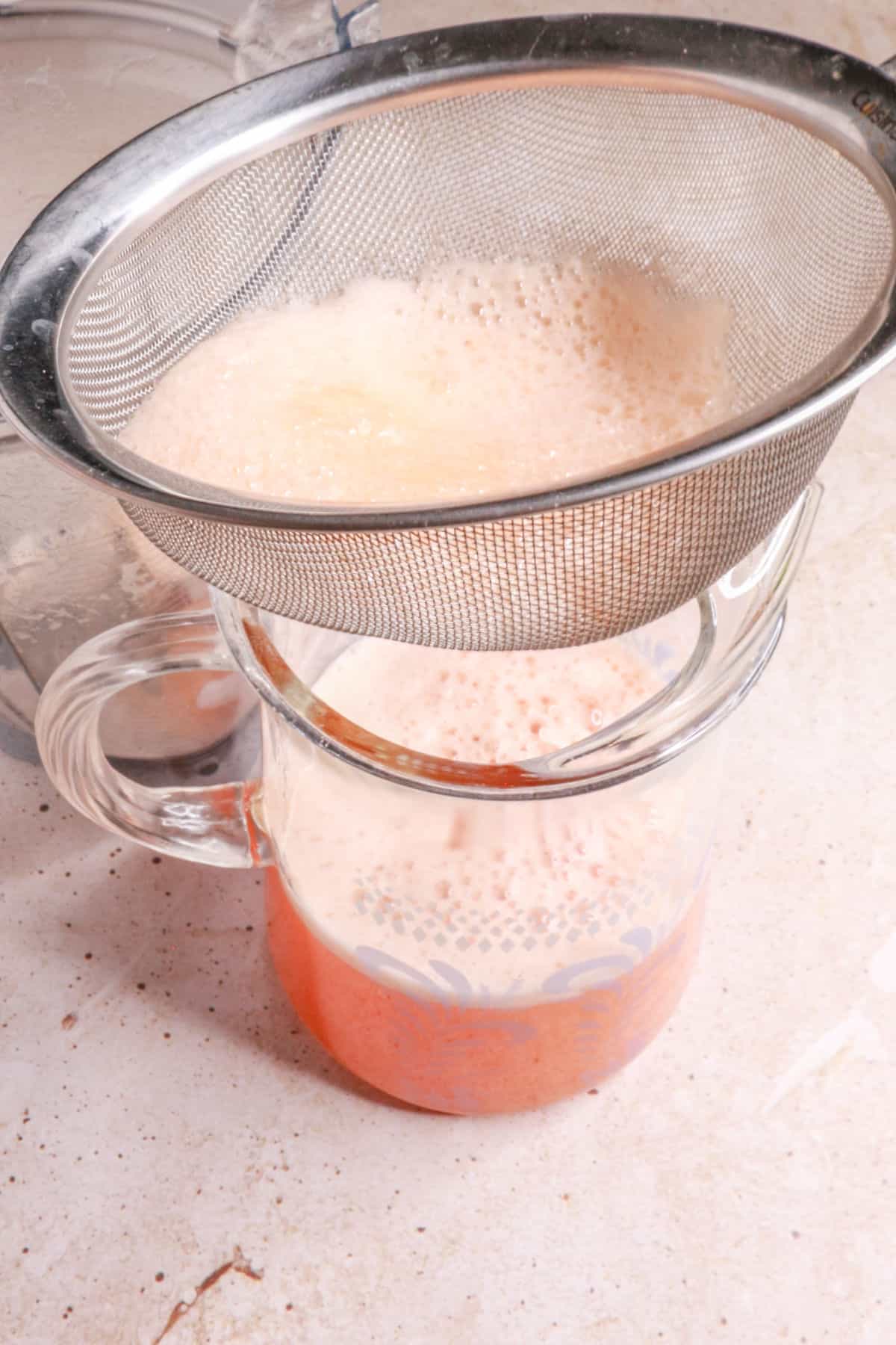 Straining agua de melon through a fine-mesh sieve into a pitcher