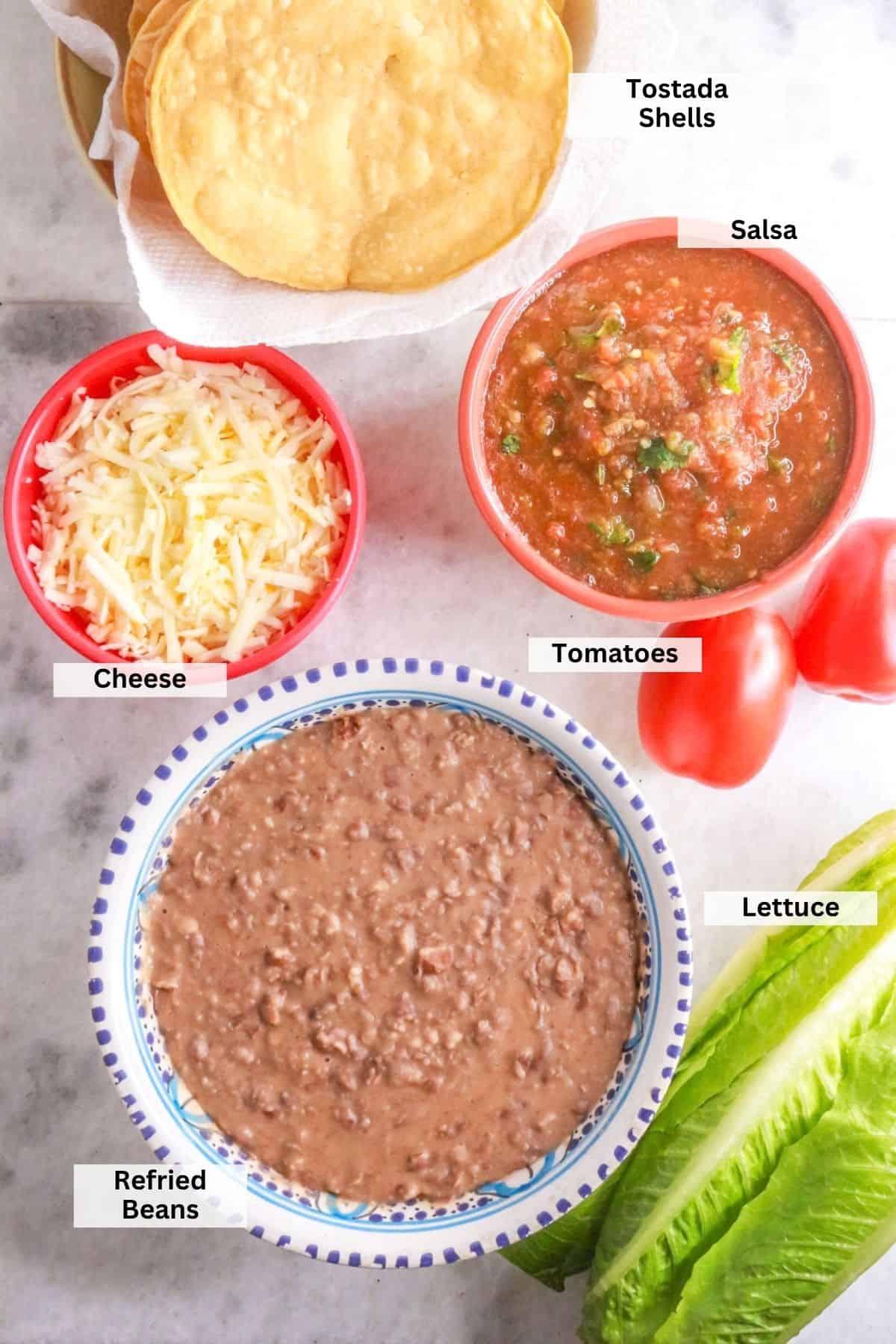 Ingredients for Tostadas de Frijoles: tostada shells, cheese, refried beans, salsa, tomatoes, lettuce